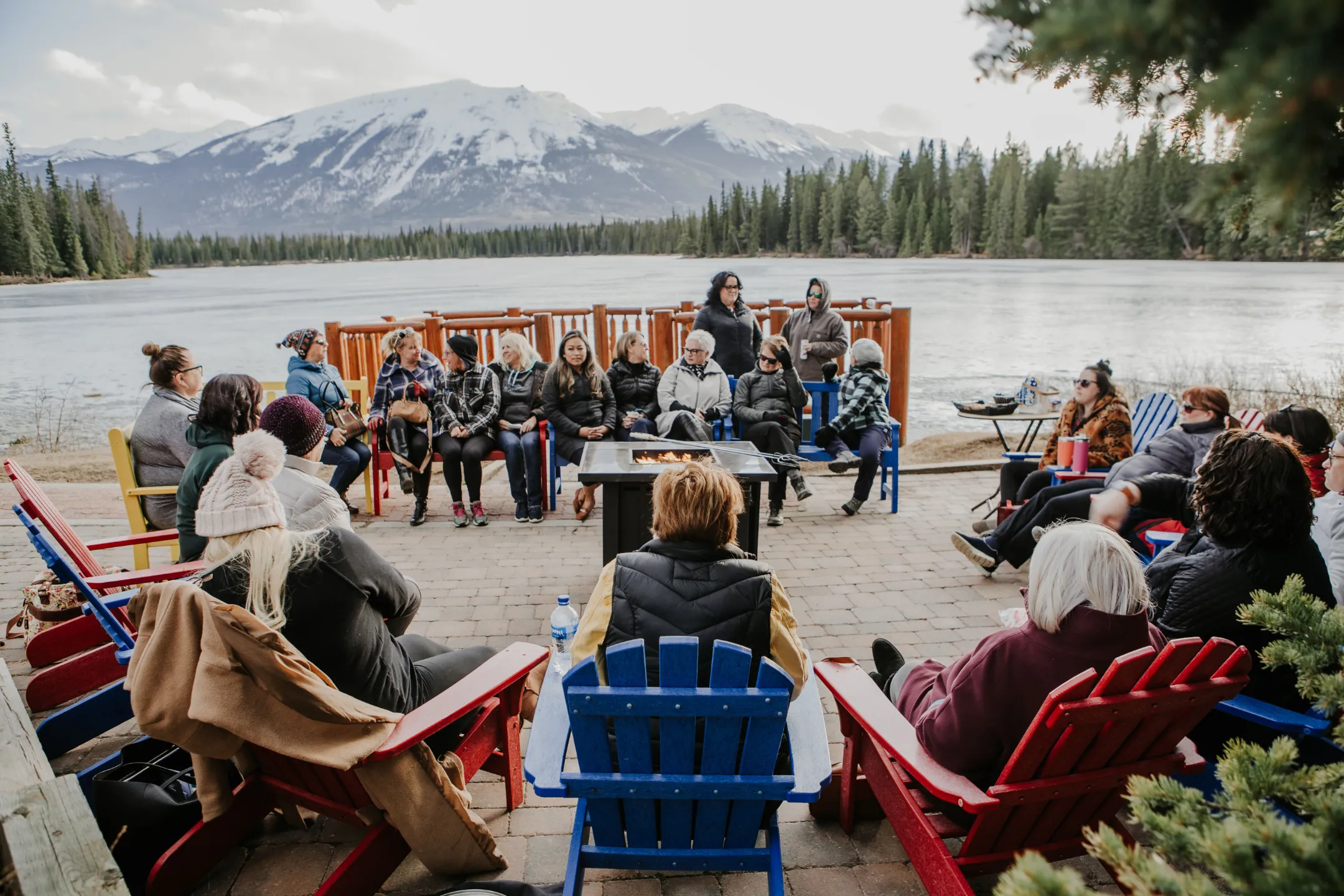 Women gathered in Adirondack chairs by a lake with the Canadian Rockies behind them at Carla's retreat